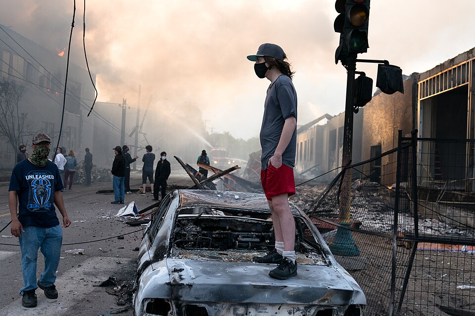 During the morning hours on May 28, 2020, a man stands casually looking northward on a burned out ca