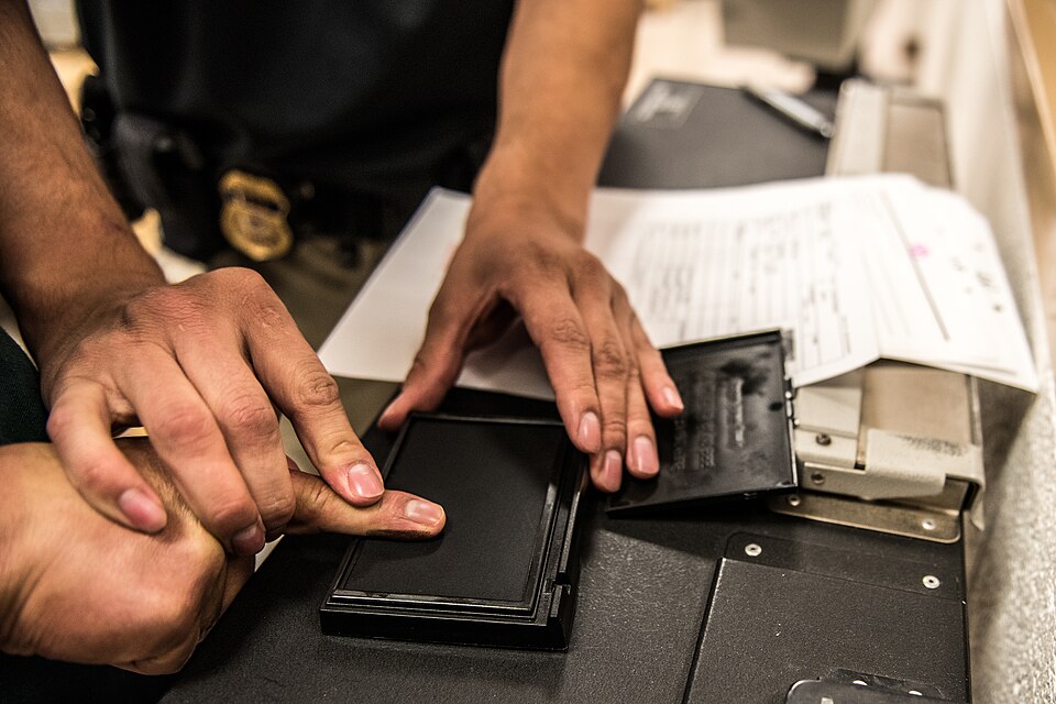 An ICE ERO officer fingerprints someone in custody at a processing center.