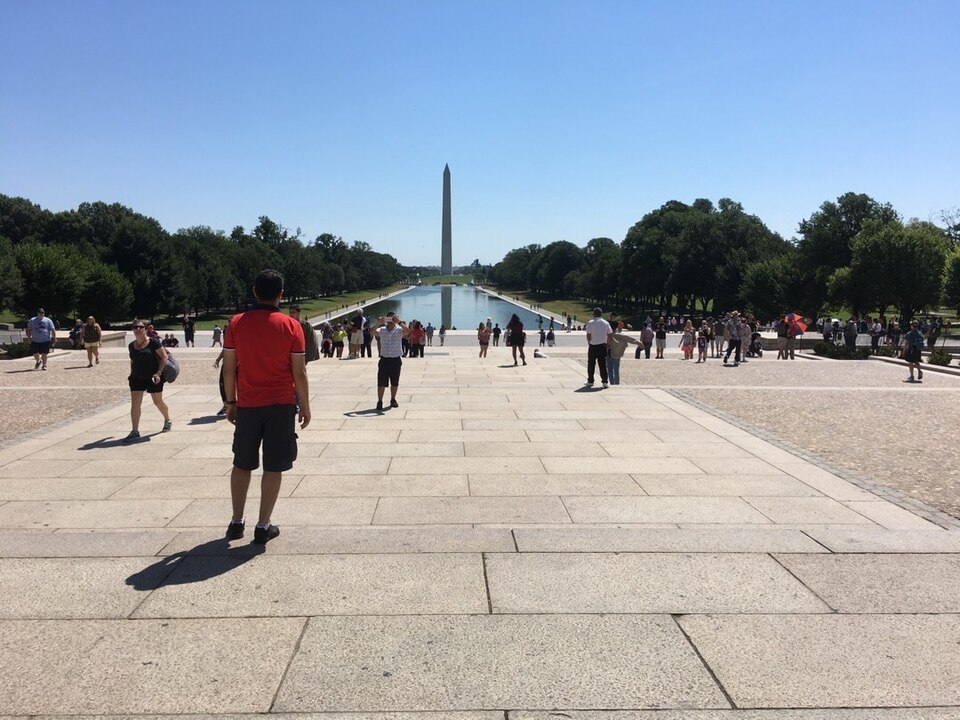 The Washington Monument is in the distance with the Reflecting Pool in front of it. Several visitors